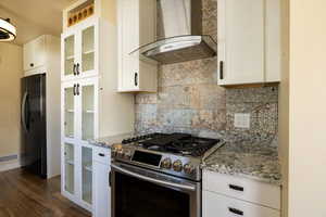 Kitchen featuring beautiful backsplash, refrigerator, white cabinets, stainless steel range with gas stovetop, and wall chimney range hood