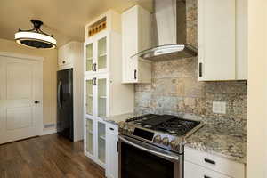 Kitchen featuring wall chimney exhaust hood, stainless steel gas range oven, glass insert cabinets, and white cabinetry