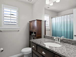 Bathroom with curtained shower, visible vents, toilet, vanity, and baseboards