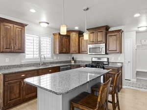 Kitchen with a kitchen island, light stone counters, stainless steel appliances, a kitchen bar, and a sink