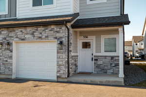 Doorway to property featuring a garage, stone siding, and roof with shingles