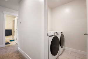 Laundry room featuring light tile patterned floors, light colored carpet, washing machine and dryer, laundry area, and baseboards