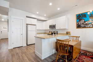 Kitchen featuring stainless steel appliances, visible vents, white cabinets, light stone countertops, and a peninsula