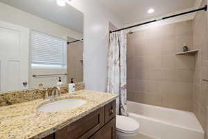 Bathroom with recessed lighting, vanity, toilet, and shower / bathtub combination with curtain