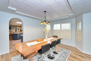 Dining area featuring arched walkways, a tray ceiling, light wood-style floors, wood ceiling, and baseboards