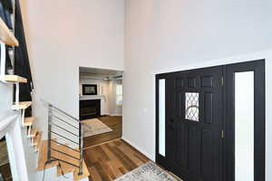 Entrance foyer with a fireplace with flush hearth, a towering ceiling, baseboards, stairway, and dark wood finished floors