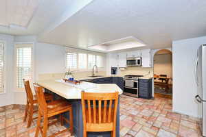 Kitchen with arched walkways, stainless steel appliances, a peninsula, a sink, and light countertops