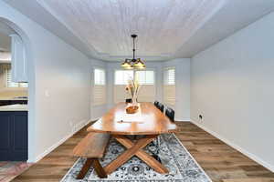 Dining room with arched walkways, dark wood finished floors, a chandelier, wooden ceiling, and baseboards