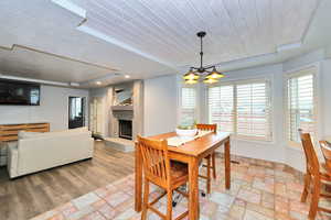 Dining room featuring a large fireplace, light wood finished floors, wood ceiling, a textured ceiling, and a notable chandelier