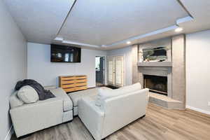 Living area featuring a large fireplace, baseboards, a raised ceiling, wood finished floors, and a textured ceiling