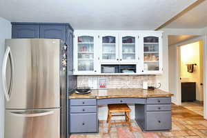 Kitchen featuring a textured ceiling, tasteful backsplash, glass insert cabinets, and freestanding refrigerator