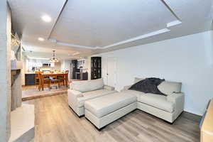 Living area featuring light wood-type flooring, a notable chandelier, a raised ceiling, and a textured ceiling