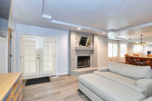 Living area with french doors, a fireplace, light wood-style floors, a textured ceiling, and baseboards