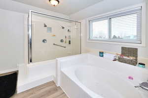 Bathroom with a textured ceiling, a stall shower, wood finished floors, and a bath