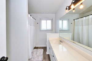 Full bathroom with baseboards, visible vents, wood finished floors, and vanity