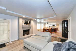 Living area with a large fireplace, baseboards, visible vents, a textured ceiling, and light wood-type flooring