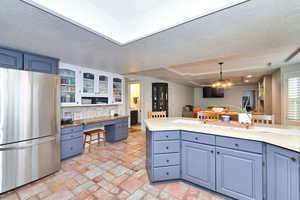 Kitchen with backsplash, glass insert cabinets, freestanding refrigerator, built in study area, and blue cabinets