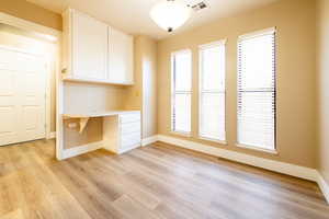 Interior space with light wood-style floors, visible vents, built in desk, and baseboards