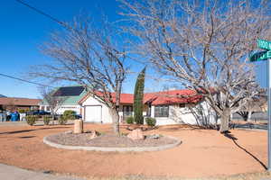 Ranch-style house featuring stucco siding, solar panels, an attached garage, driveway, and a tiled roof