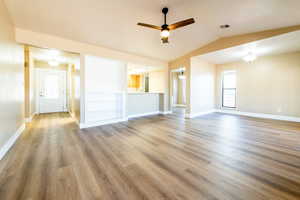 Unfurnished living room featuring a ceiling fan, lofted ceiling, baseboards, and wood finished floors