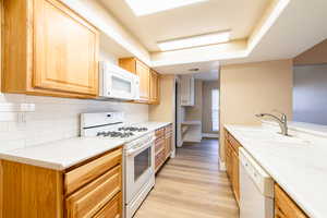 Kitchen with white appliances, a sink, light wood-style floors, light countertops, and decorative backsplash