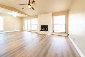 Unfurnished living room featuring baseboards, visible vents, lofted ceiling, wood finished floors, and a brick fireplace