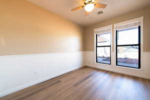 Spare room with a wainscoted wall, a ceiling fan, visible vents, and wood finished floors