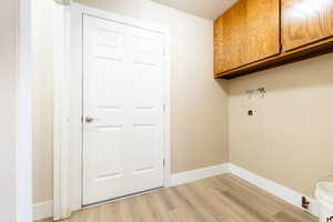 Clothes washing area with cabinet space, light wood-style flooring, hookup for a washing machine, and baseboards