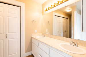 Full bathroom with double vanity, a closet, baseboards, and a sink