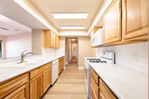 Kitchen featuring white appliances, a sink, light wood finished floors, and light brown cabinetry