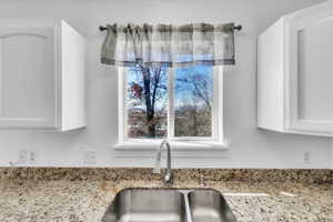 Interior details with a sink, white cabinetry, and light stone countertops