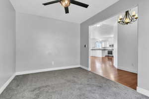 Unfurnished room featuring dark colored carpet, baseboards, and ceiling fan with notable chandelier