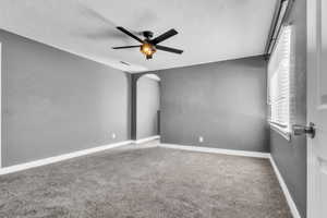 Carpeted spare room with arched walkways, a textured ceiling, a ceiling fan, and baseboards