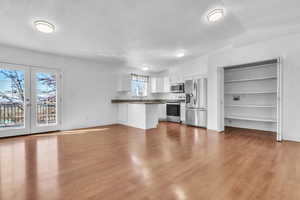 Kitchen featuring stainless steel appliances, dark countertops, white cabinets, wood finished floors, and a peninsula