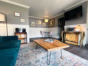 Living room with dark wood-style floors, a textured ceiling, a wainscoted wall, and crown molding