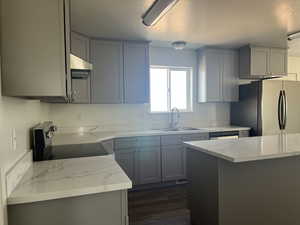 Kitchen featuring a sink, freestanding refrigerator, light stone countertops, stainless steel electric range, and under cabinet range hood
