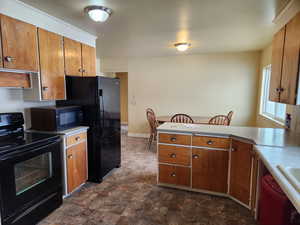 Kitchen with light countertops, brown cabinetry, stone finish flooring, a peninsula, and black appliances