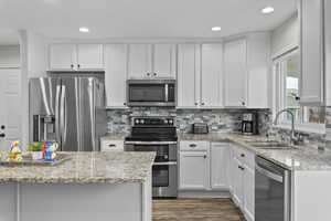 Kitchen featuring stainless steel appliances, dark wood-style flooring, a sink, white cabinets, and decorative backsplash