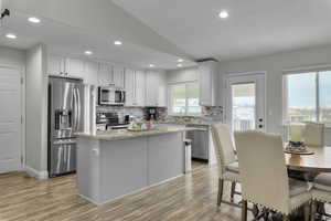 Kitchen featuring light wood-style flooring, stainless steel appliances, vaulted ceiling, a center island, and tasteful backsplash