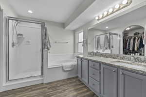 Full bathroom featuring double vanity, wood finished floors, a stall shower, and a sink