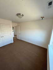 Unfurnished bedroom featuring dark colored carpet, a closet, visible vents, and baseboards