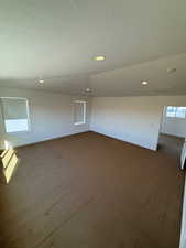 Spare room featuring a textured ceiling, dark colored carpet, and baseboards