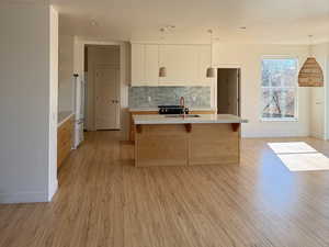 Kitchen featuring a breakfast bar, a sink, light countertops, light wood finished floors, and tasteful backsplash