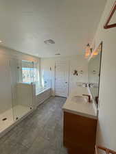 Bathroom featuring double vanity, a garden tub, a textured ceiling, a shower stall, and a sink