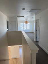 Hallway featuring carpet, baseboards, a textured ceiling, and an upstairs landing