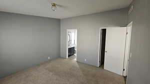 Unfurnished bedroom with light colored carpet, visible vents, and ensuite bath