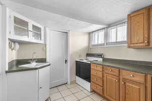 Kitchen with dark countertops, white electric stove, a sink, and light tile patterned floors