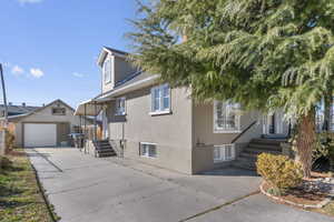 View of front of home featuring roof with shingles, a detached garage, stucco siding, concrete driveway, and an outdoor structure