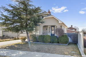 View of front facade featuring a porch, a chimney, fence, and stucco siding