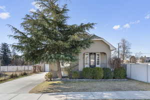 View of property hidden behind natural elements featuring driveway, covered porch, fence, and stucco siding